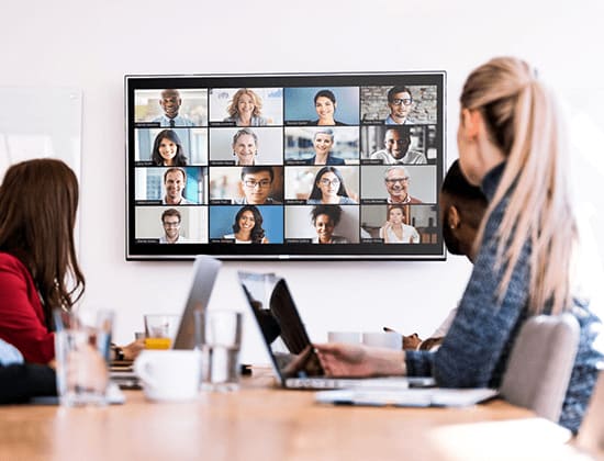 Personal i ett mötesrum tittar på en skärm med en pågående videokonferens